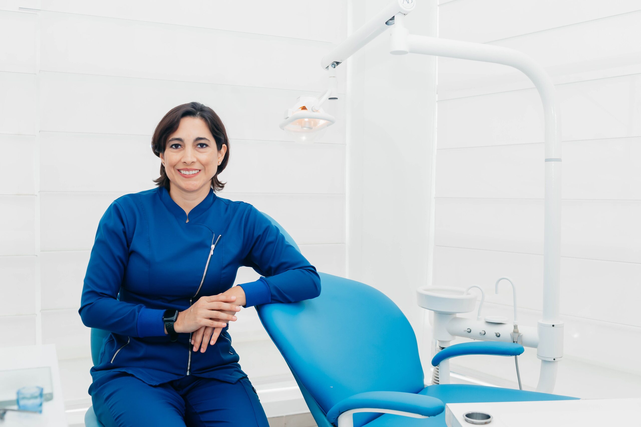 Our Services Smiling female dentist sitting in a modern clinic, ready for patients