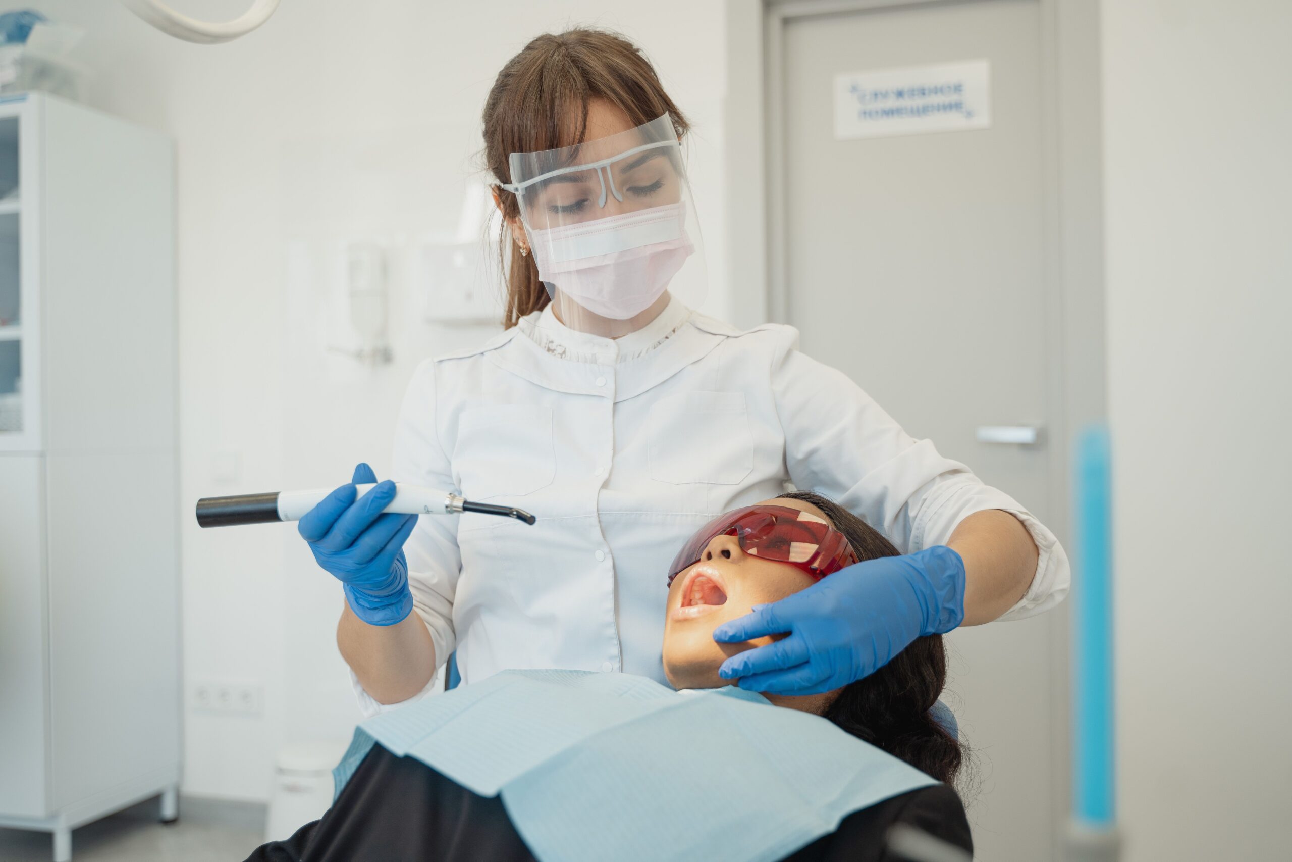 Our Services A female dentist using curing light on a patient in a modern dental clinic.