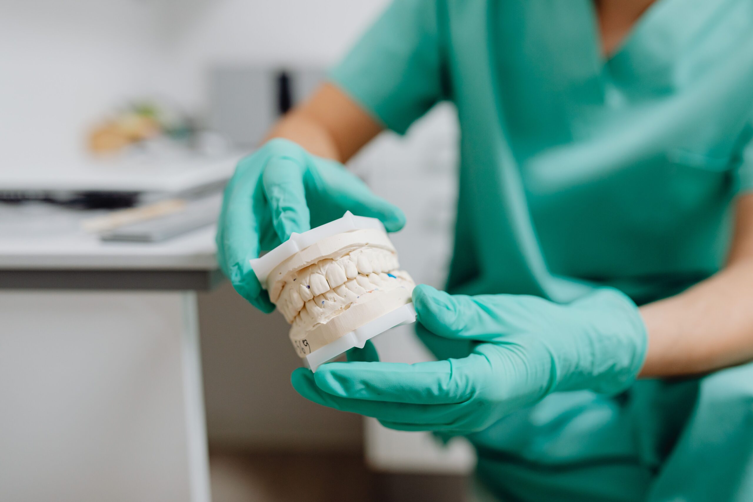 Our Services A close-up of hands in latex gloves holding a dental cast in a dental office.