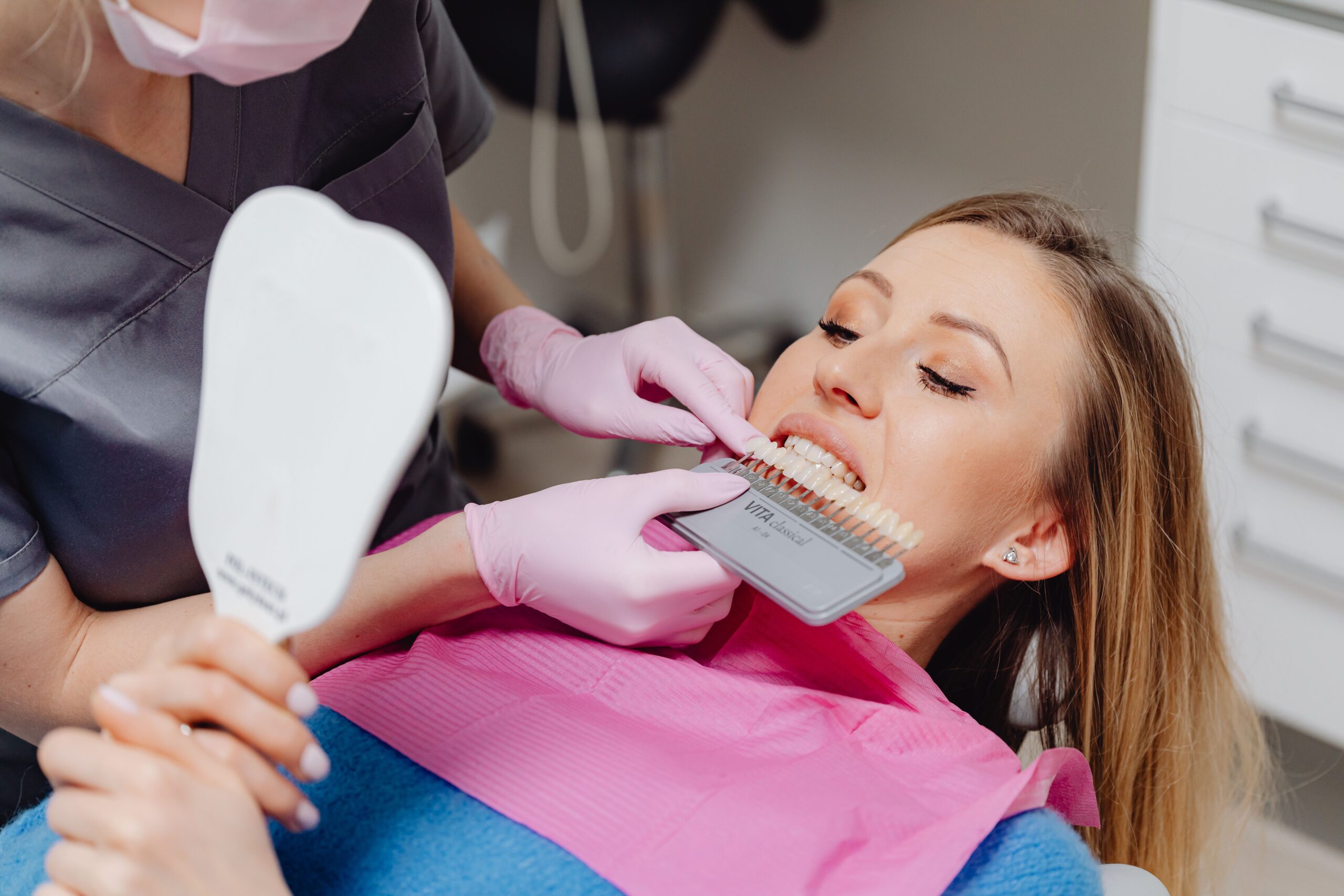 Our Services Dentist using a shade guide to match tooth color for a patient in a dental clinic.