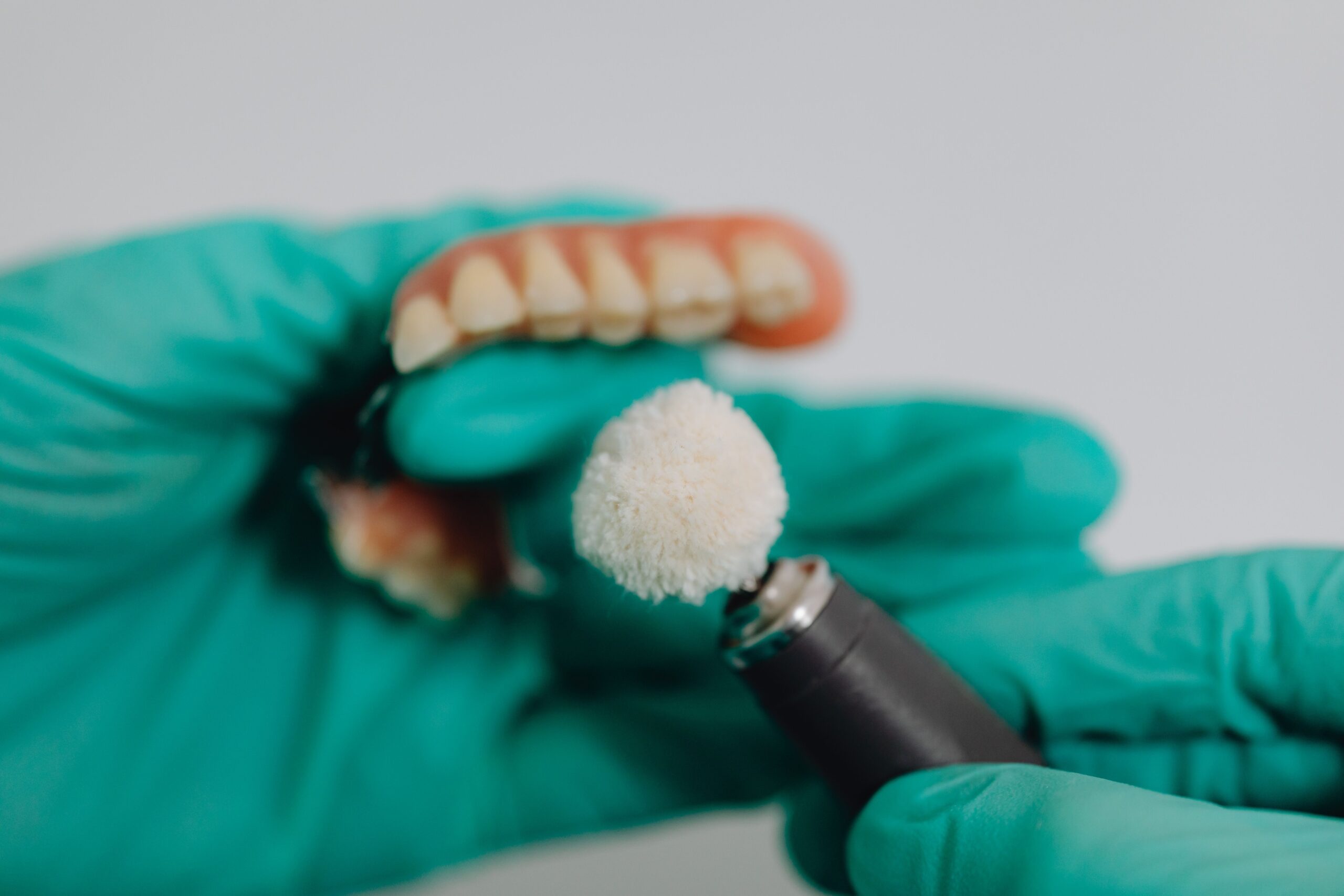 Our Services Detailed image of dentures being polished by a dental professional wearing gloves. Ideal for dental care topics.