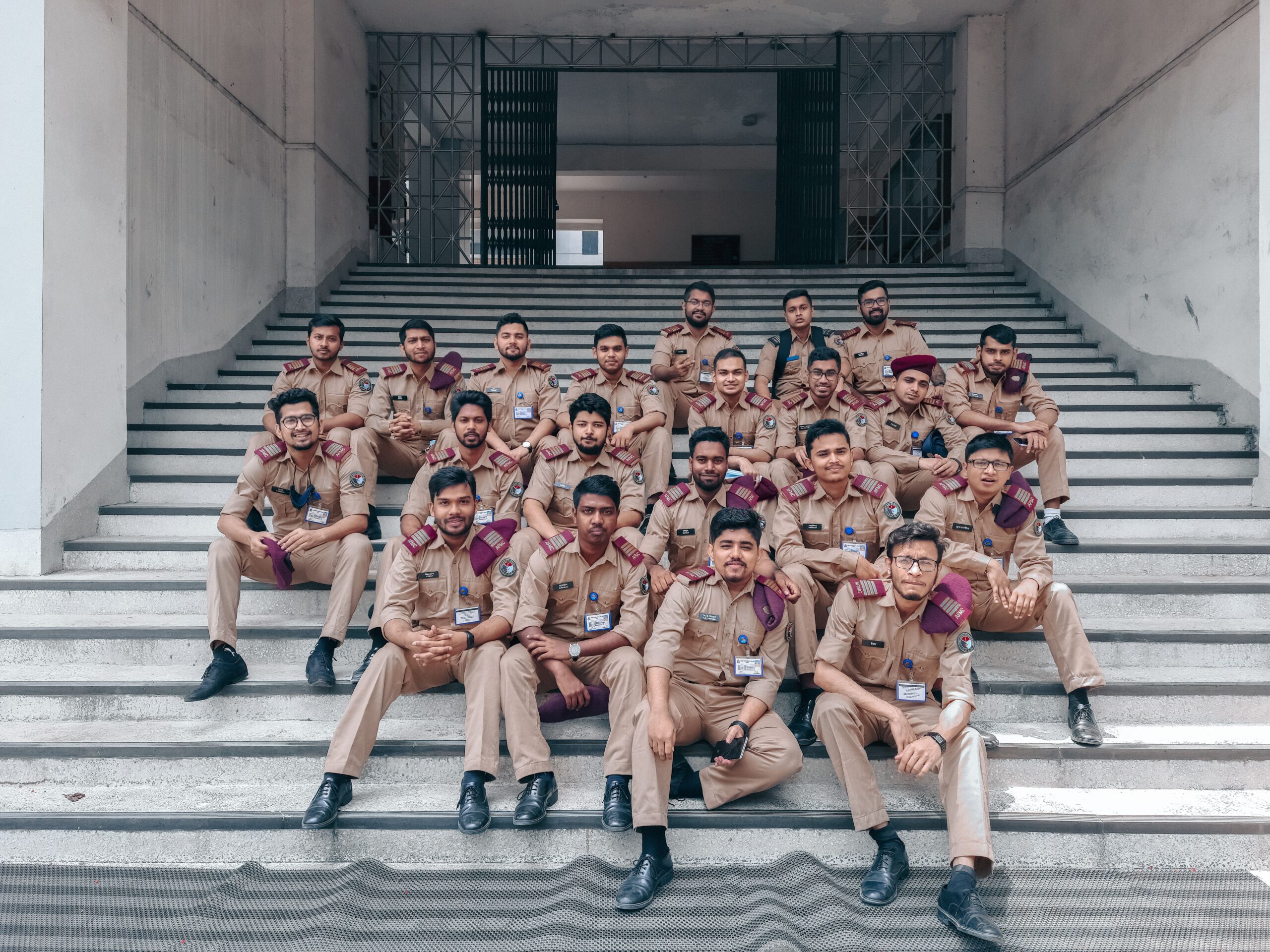 A group of men in military-style uniforms sitting on stairs outdoors in Dhaka, Bangladesh.