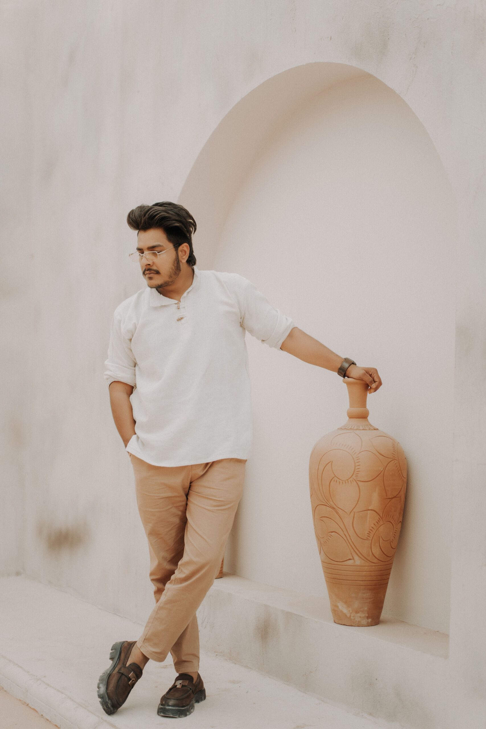 Fashionable man in smart casual wear poses with a clay vase in an elegant, minimalistic setting.